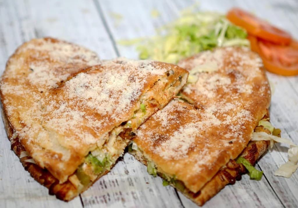 Heart-shaped stuffed flatbread topped with powdered cheese, served with lettuce and tomato