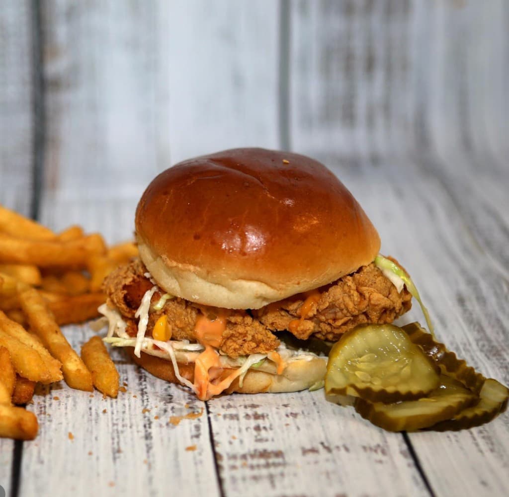 Crispy chicken sandwich on a brioche bun with slaw, sauce, fries, and pickle chips
